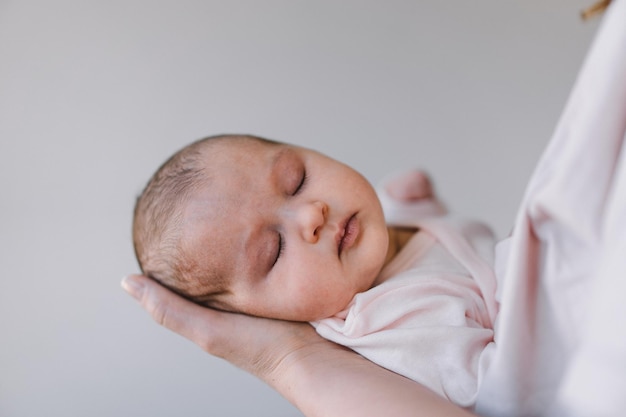 Portrait of baby sweet sleeping on mother's hands Loving mom carying of her newborn baby at home Mother hugging her little 1 months old girl