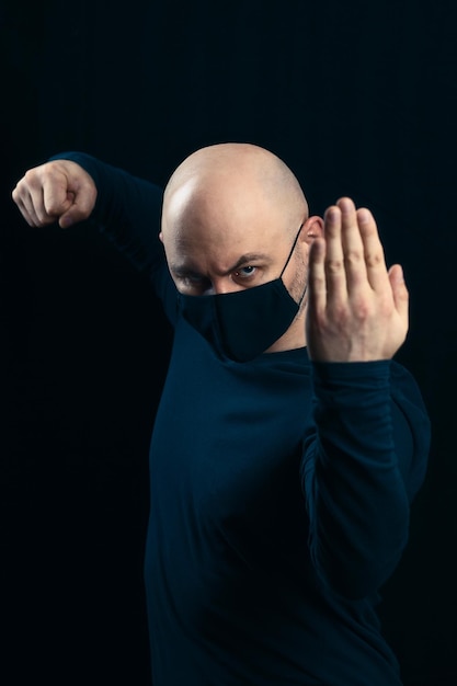 어두운 배경에 검은 의료 마스크를 쓴 대머리 남자의 초상화 질병과 바이러스에 대한 위협적인 제스처