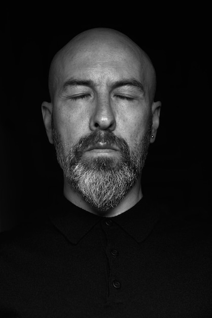 Photo portrait of a bald man with a beard and with closed eyes closeup on a black background