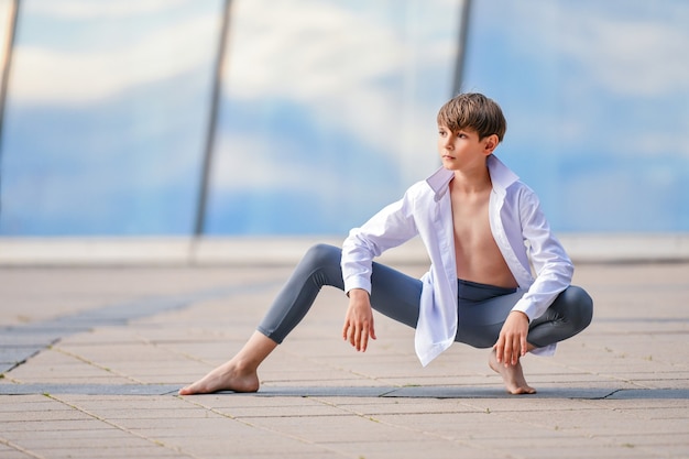 Foto ritratto di un ragazzo di balletto che si esercita sullo sfondo del riflesso del cielo nella parete di vetro