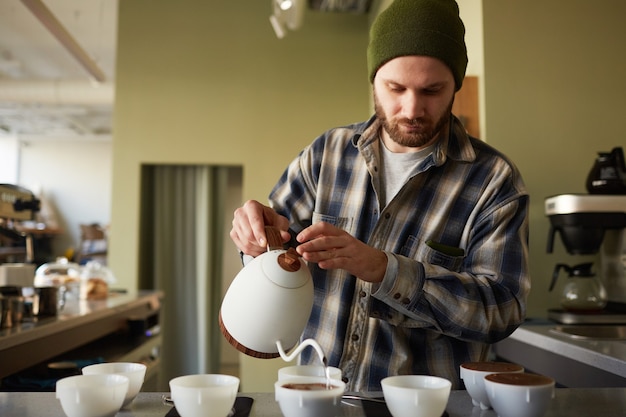 Photo portrait of bearded barista pouring coffee to cups in row while standing at bar, copy space