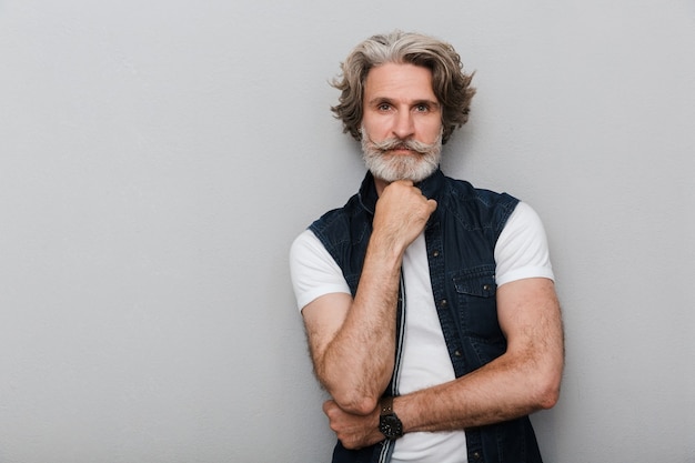 Portrait of a bearded concentrated handsome senior man with grey hair isolated over grey wall background.