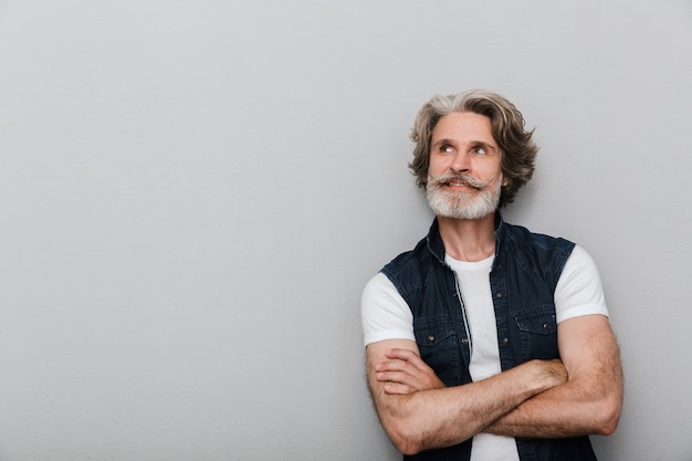 Portrait of a bearded dreaming pleased optimistic senior man grey hair isolated over grey wall background.