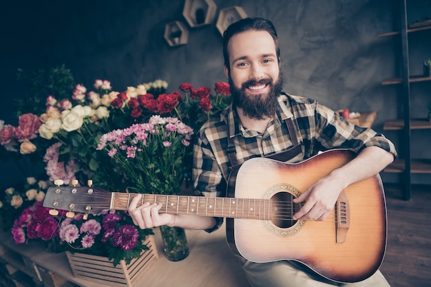 Ritratto di barbuto fioraio in posa nel suo negozio di fiori con la chitarra