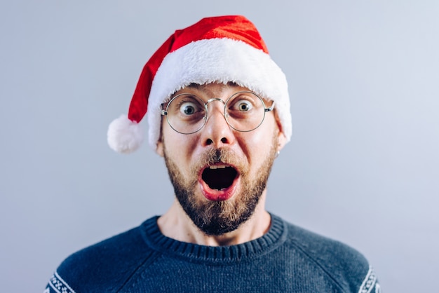 Portrait of a bearded guy in santa hat and eyeglasses looking astonished