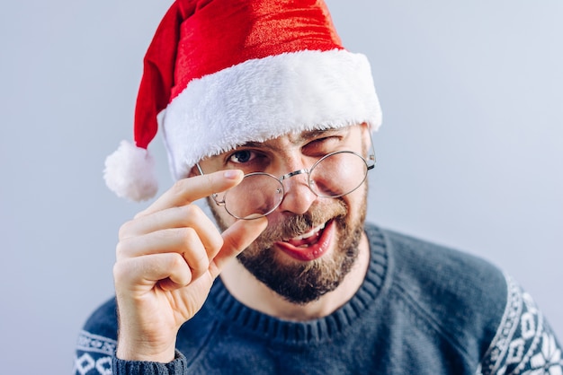 Portrait of a bearded guy in santa hat and eyeglasses smiling and winking directly at the camera
