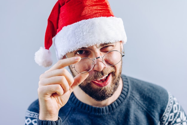 Foto ritratto di un ragazzo barbuto in santa cappello e occhiali da vista sorridente e ammiccante direttamente alla telecamera