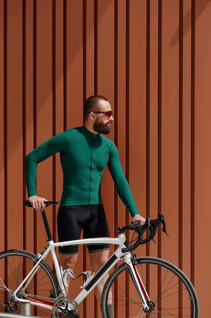 Портрет бородатого парня с велосипедом, позирующего на оранжевом фоне стены