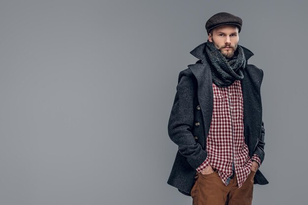 Photo portrait of a bearded hipster man dressed in a gray jacket and a wool cap isolated on grey background.