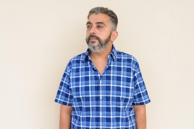 Portrait of bearded Indian businessman thinking against plain background