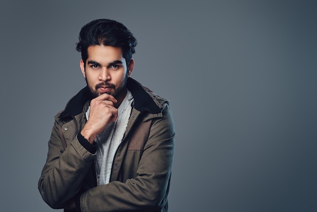 Portrait of bearded Indian male dressed in a winter jacket over grey background.