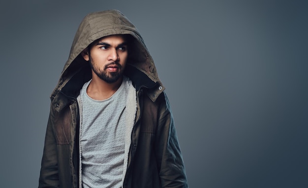 Portrait of bearded Indian male dressed in a winter jacket over grey background.