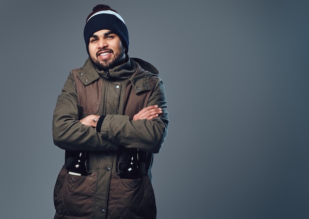 Portrait of bearded Indian male dressed in a winter jacket over grey background.