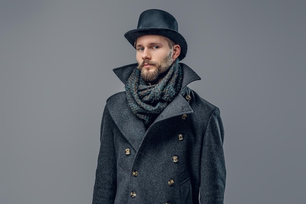 Portrait of bearded male dressed in a grey jacket and a hat isolated on grey background.