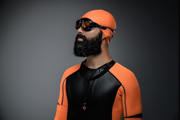 Portrait of bearded male in scuba diving mask and orange neopren diving suit isolated on grey background.