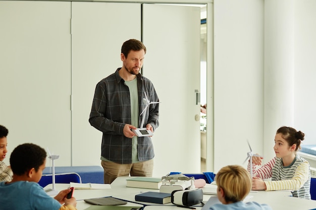 Portrait of bearded male teacher demonstrating project to kids in robotics class copy space