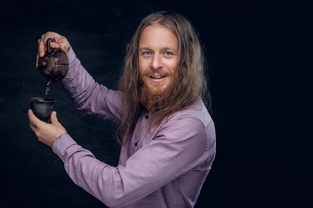 Portrait of bearded male with long hair pours tea.