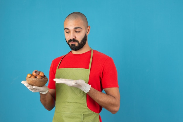 Portrait of a bearded man in apron holding a wooden bowl of dried fruits . 