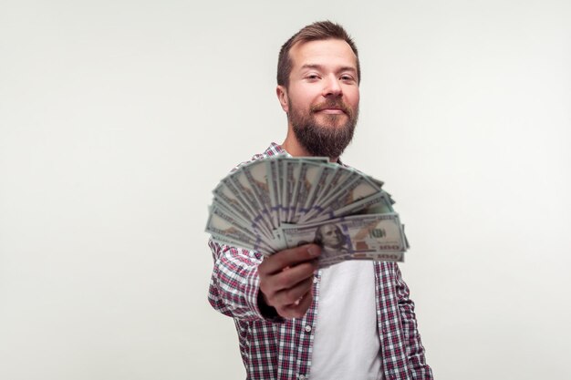 Портрет бородатого мужчины в повседневной клетчатой рубашке, высокомерно смотрящего в камеру и показывающего деньги, отдающего доллары в камеру, довольного большим доходом, выигрышем в лотерею. студийный снимок на белом фоне