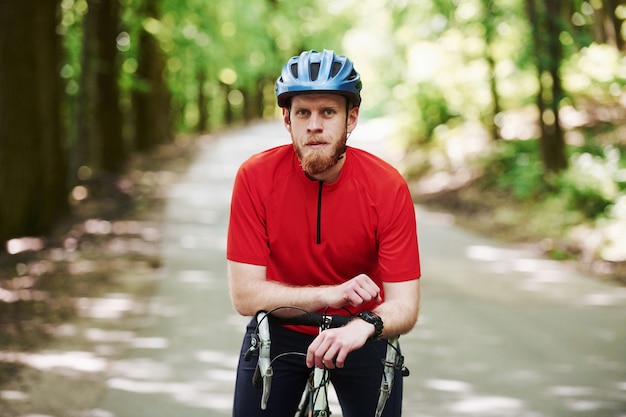 Portrait of bearded man. Cyclist on a bike is on the asphalt road in the forest at sunny day