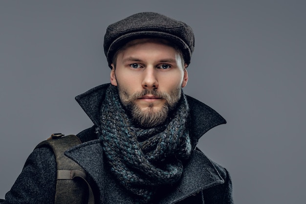 Portrait of a bearded man dressed in a worm jacket and wool cap isolated on grey background.