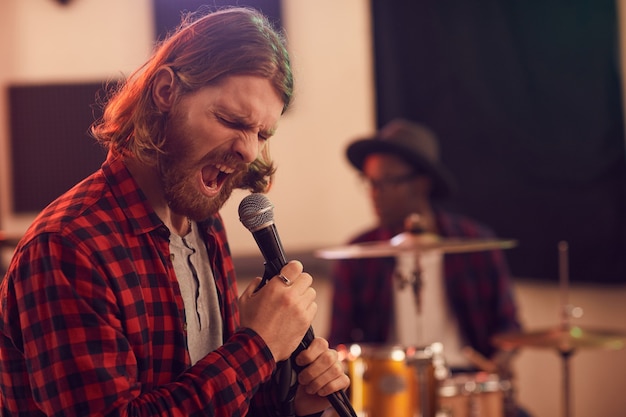 Portrait bearded man screaming to microphone while playing music during rehearsal