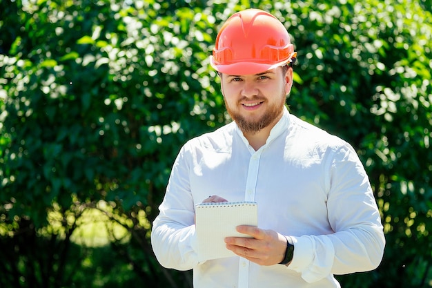 Foto ritratto di un uomo barbuto in camicia bianca e elmetto da costruzione. uomo d'affari nel parco