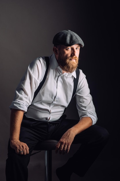 Portrait on a bearded man in white shirt and suspenders on black background in studio