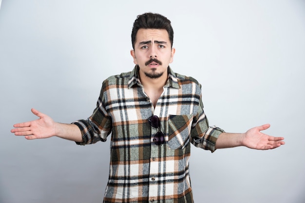 Portrait of bearded man with glasses asking what's up over white wall.