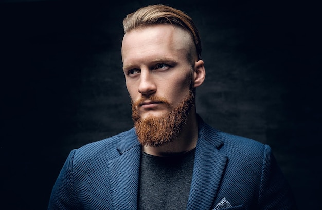 Portrait of bearded redhead hipster male dressed in a blue jacket over grey background.