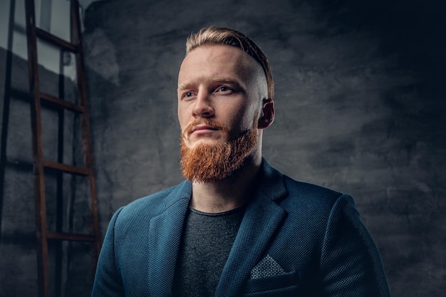 Portrait of bearded redhead hipster male dressed in a blue jacket over grey background.