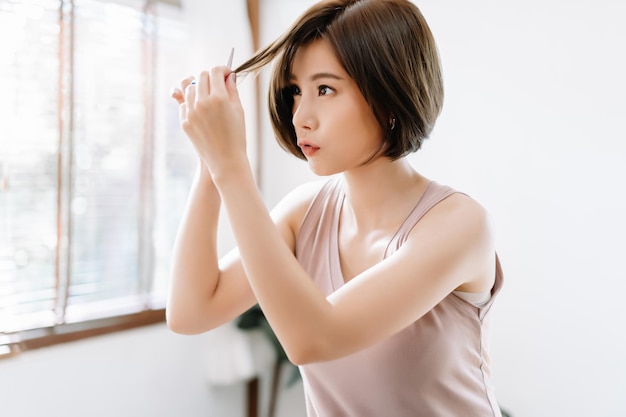 Portrait of beauiful young Asian woman having her hair cut with scissors at home She's stay at home during the coronavirus pandemic Self hair care during quarantine