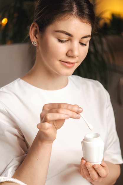 Foto ritratto di un'estetista che raccoglie la crema con una spatola da un barattolo pronto per applicarla sul viso della donna test e pubblicità di prodotti cosmetici per la cura