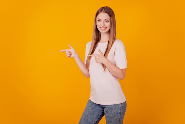 Portrait of beautiful adorable lady presenting empty blank space with fingers on yellow background