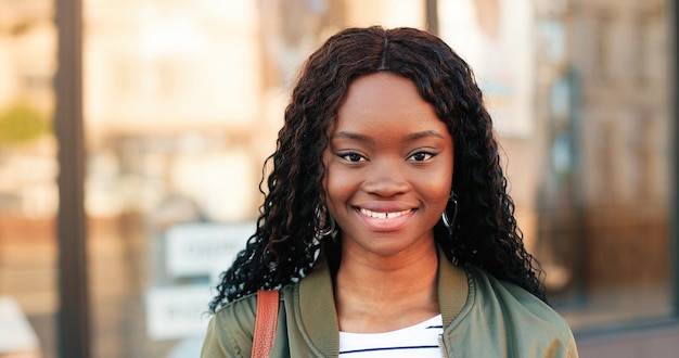 Portrait of beautiful African American girl with curly brunette hair standing on the warm spring city street dressed at the casual clothes during morning.