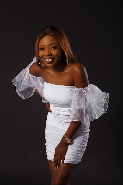 Portrait of a beautiful african american woman in short white dress smiling on black background