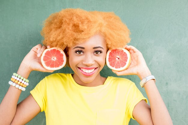 Photo portrait of a beautiful african woman with grapefruit slices on the green wall background