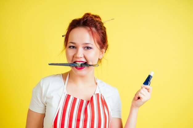 Portrait of a beautiful artist in an apron holding a palette and brush on a yellow background in the studio . inspiration and muse idea