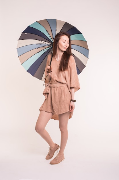 Portrait of beautiful asian brunette female standing under umbrella over white wall