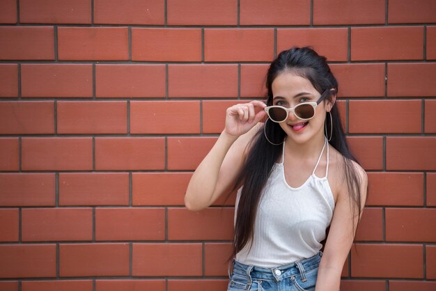 Portrait of beautiful asian chic girl pose for take a picture on brick wall backgroundLifestyle of teen thailand peopleModern woman happy conceptPunk rock style