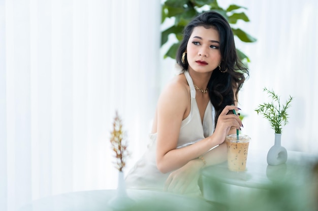 Ritratto bella freelance asiatica modello di moda donna d'affari di persone di successo in abito bianco senza maniche estivo e caffè in tazza nella caffetteria