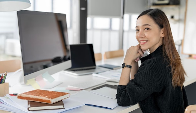 Portrait of Beautiful Asian freelancer Using Desktop Computer at home office Smiling and looking at camera