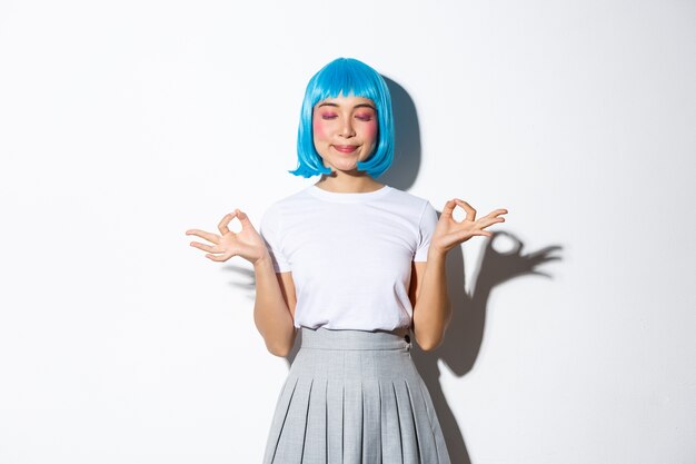 Portrait of beautiful asian girl in blue wig meditating, looking peaceful and smiling with eyes closed