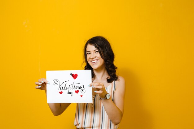Portrait of A beautiful Asian girl holding a white blank in her hands with her heart over yellow wall