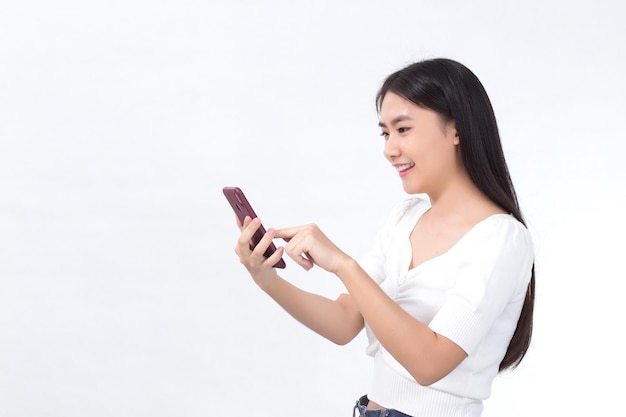 Портрет красивой азиатской девушки с удовольствием пользуйтесь смартфоном на белом фоне