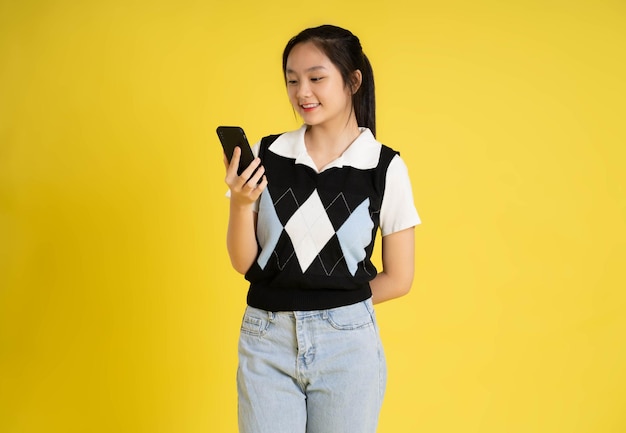 Portrait of a beautiful asian girl using phone on a yellow background