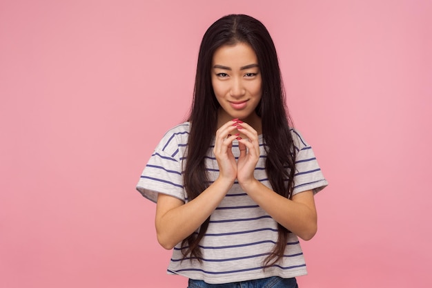 Portrait of beautiful asian girl with long brunette hair scheming evil idea and looking at camera with slyly expression having tricky devious plan in mind studio shot isolated on pink background