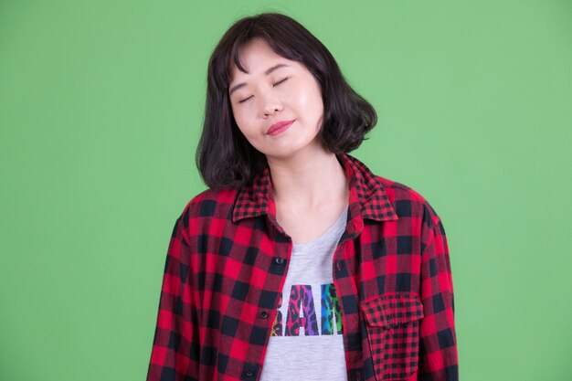 Portrait of beautiful Asian hipster woman with short hair against chroma key or green wall