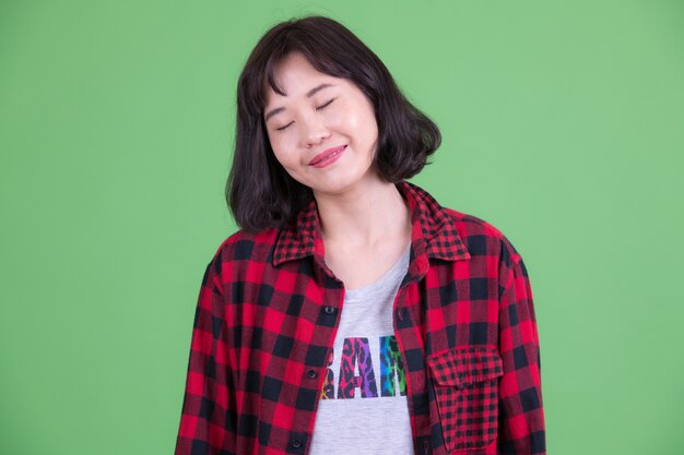 Portrait of beautiful Asian hipster woman with short hair against chroma key or green wall
