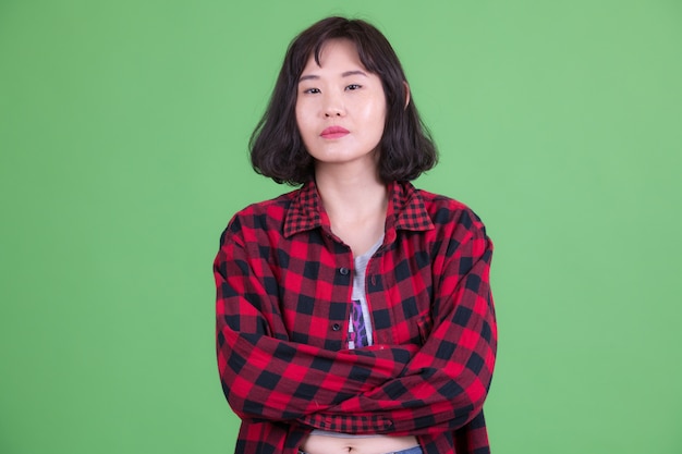 Портрет красивой азиатской хипстерской женщины с короткими волосами на фоне цветного ключа или зеленой стены